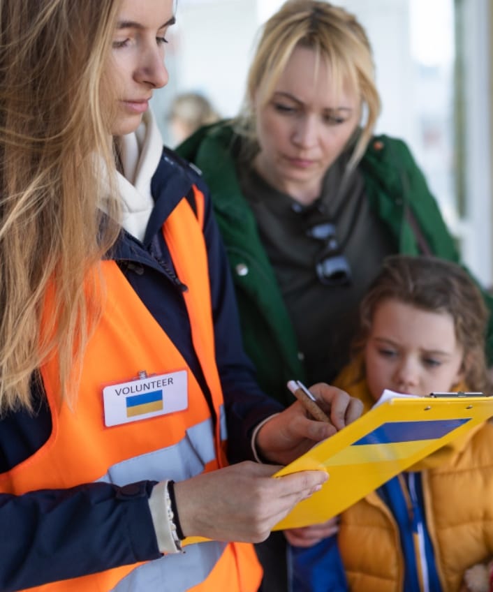 Un travailleur humanitaire tient un presse-papiers tandis qu'une mère et son enfant le regardent.