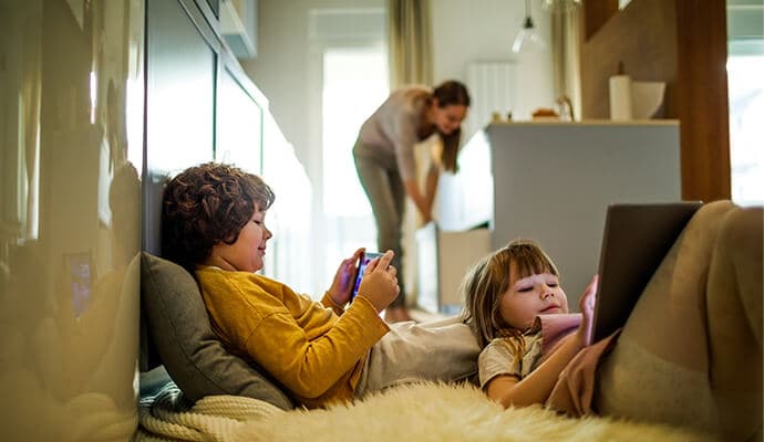 Enfants qui utilisent des tablettes avec leur mère en arrière-plan