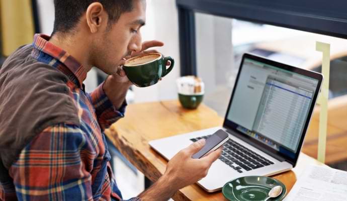 Homme buvant un café tout en regardant son téléphone.