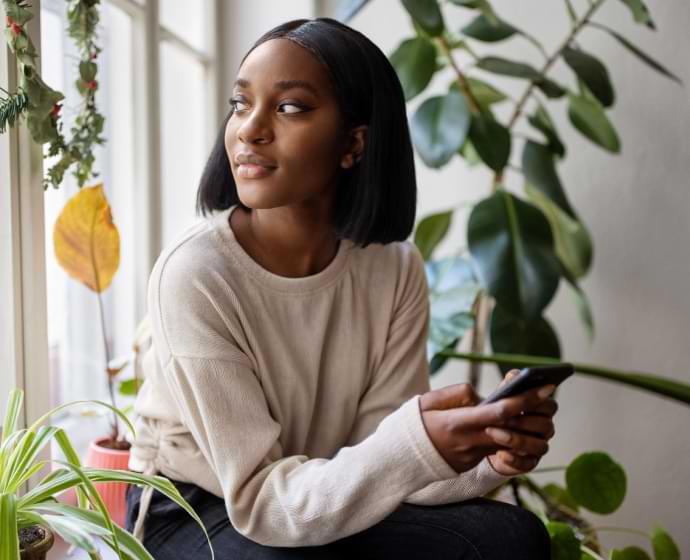 Femme regardant par une fenêtre tout en tenant un téléphone portable dans ses mains